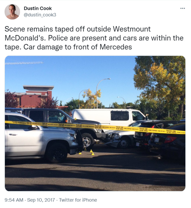 A screenshot of a tweet by user Dustin Cook (@dustin_cook3) showing a taped-off crime scene, with a white sedan crashed front bumper-to-bumper with a black van. Text reads "Scene remains taped off outside Westmount McDonald's. Police are present and cars are within the tape. Car damage to front of Mercedes"