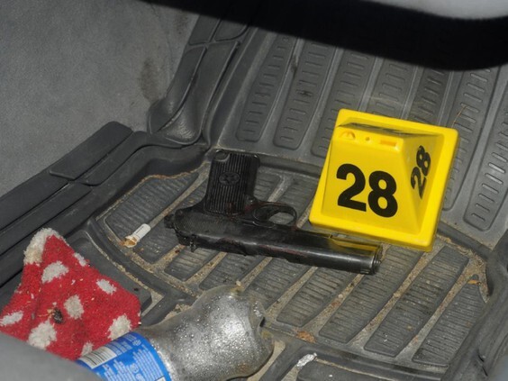 A photo of a handgun on the floor mat of a car, beside a yellow evidence marker