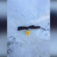 A photo of a rifle-style gun lying in the snow with a yellow crime scene card labelled "1" next to it.