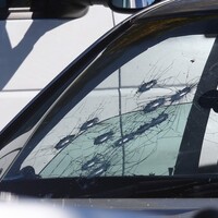 A photo of what appears to be the passenger side of the front windshield of a white vehicle; 11 bullet holes are visible in the windshield.