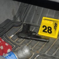 A photo of a handgun on the floor mat of a car, beside a yellow evidence marker